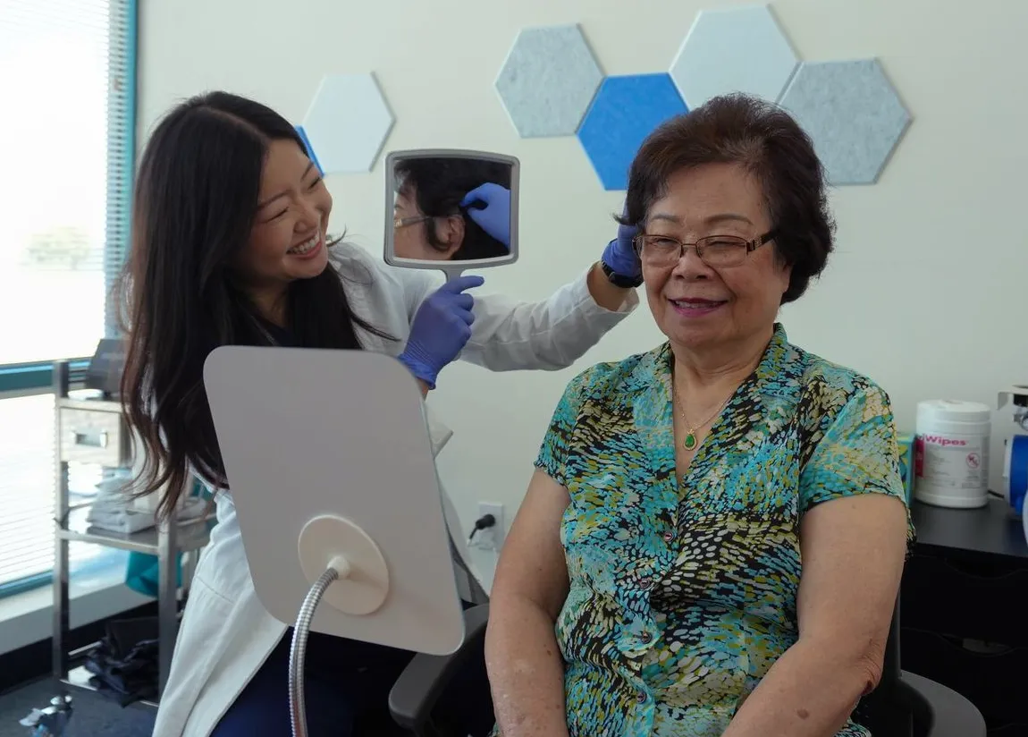 Dr. Kun checking a patient's hearing aid, showing the fitting in a hand mirror at Kun Hearing